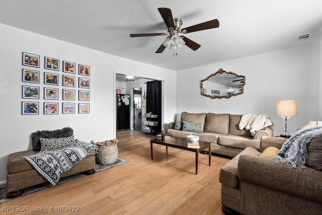 living room featuring hardwood / wood-style flooring, ceiling fan, and washer / dryer