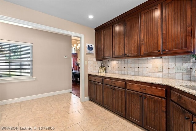 kitchen featuring light stone countertops, an inviting chandelier, backsplash, dark brown cabinets, and light tile patterned floors