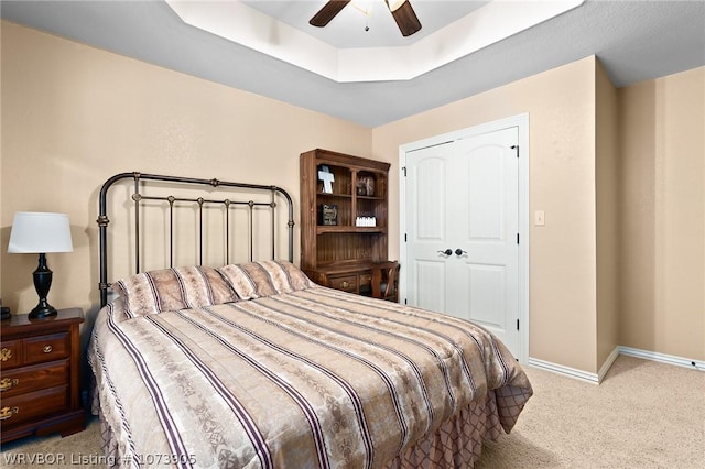 bedroom with a raised ceiling, ceiling fan, light colored carpet, and a closet