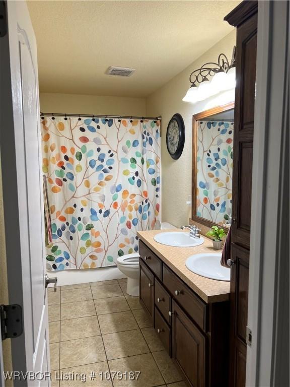 bathroom featuring double vanity, toilet, a sink, a textured ceiling, and tile patterned flooring