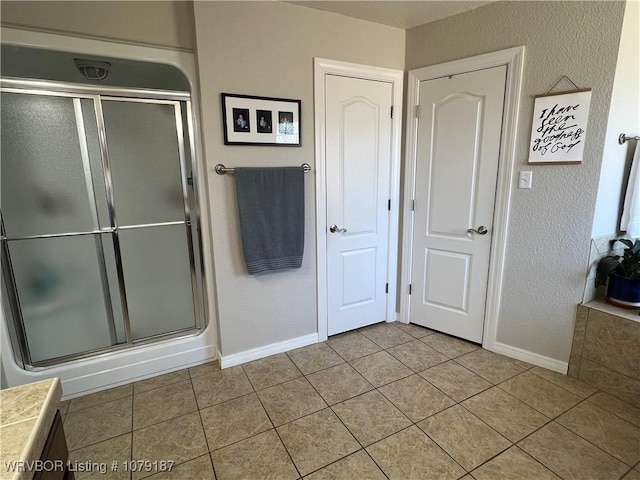 full bath with a stall shower, tile patterned flooring, and baseboards