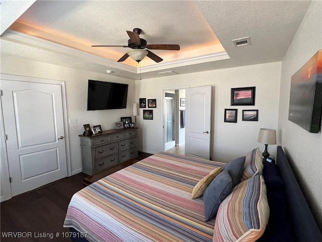 bedroom featuring visible vents, a raised ceiling, ceiling fan, dark wood-style flooring, and a textured ceiling