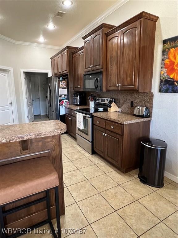 kitchen featuring dark brown cabinetry, light tile patterned floors, appliances with stainless steel finishes, ornamental molding, and backsplash