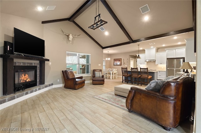 living room featuring beamed ceiling, high vaulted ceiling, a tile fireplace, and light hardwood / wood-style flooring