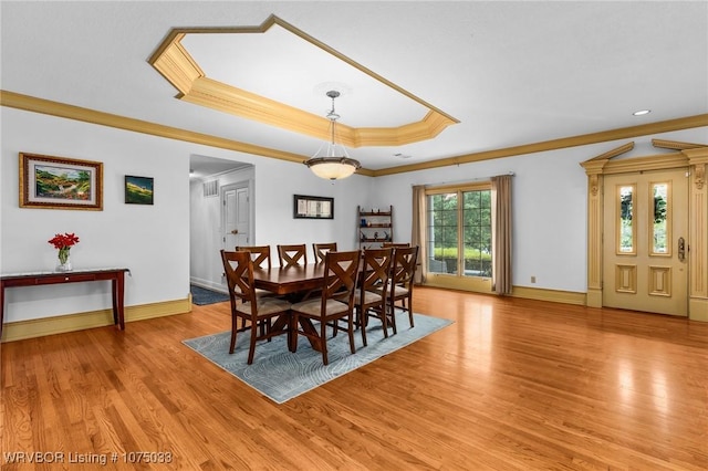 dining area with a raised ceiling, ornamental molding, and light hardwood / wood-style flooring