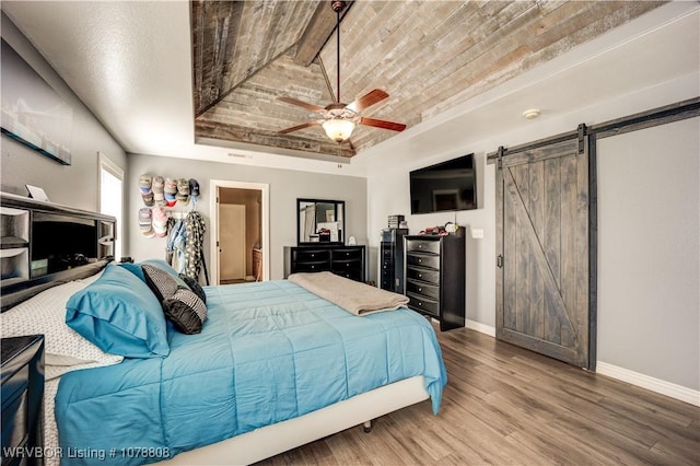 bedroom featuring ceiling fan, wood-type flooring, a barn door, wooden ceiling, and a raised ceiling