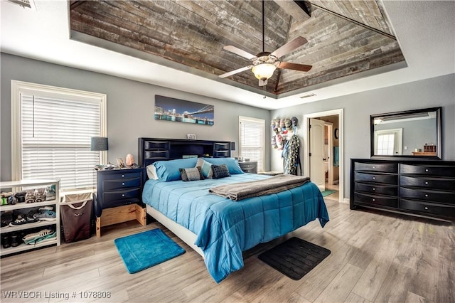 bedroom featuring connected bathroom, a raised ceiling, ceiling fan, and light wood-type flooring