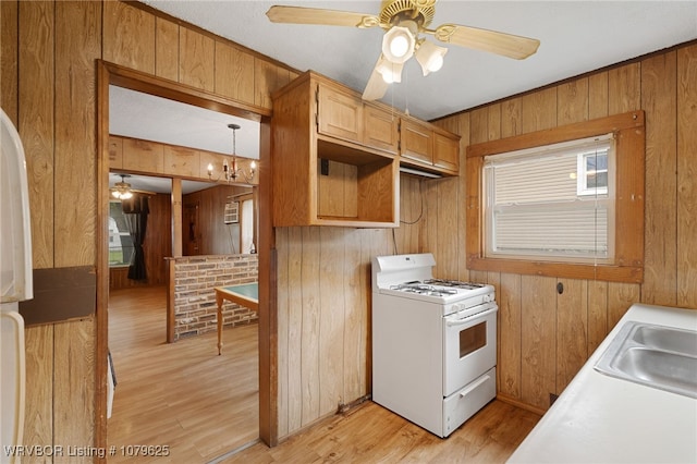 kitchen featuring wooden walls, a ceiling fan, white gas stove, a sink, and light wood-style floors