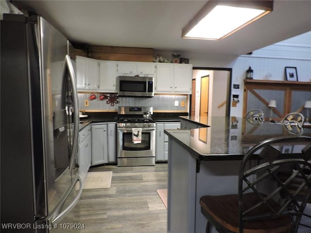 kitchen featuring white cabinetry, stainless steel appliances, a kitchen breakfast bar, light hardwood / wood-style floors, and kitchen peninsula