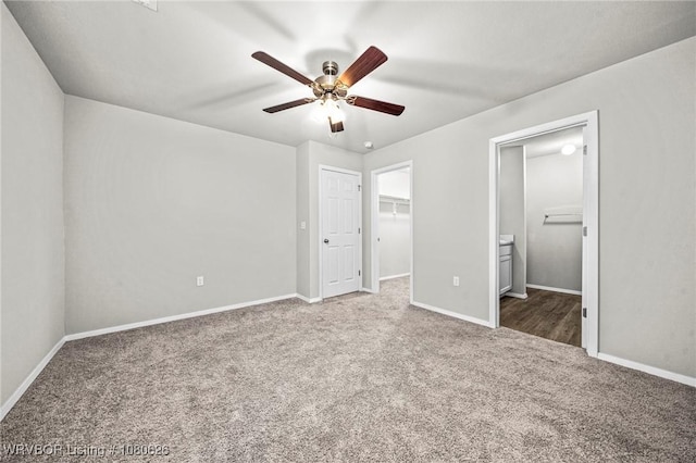 unfurnished bedroom with baseboards, a walk in closet, ceiling fan, connected bathroom, and carpet