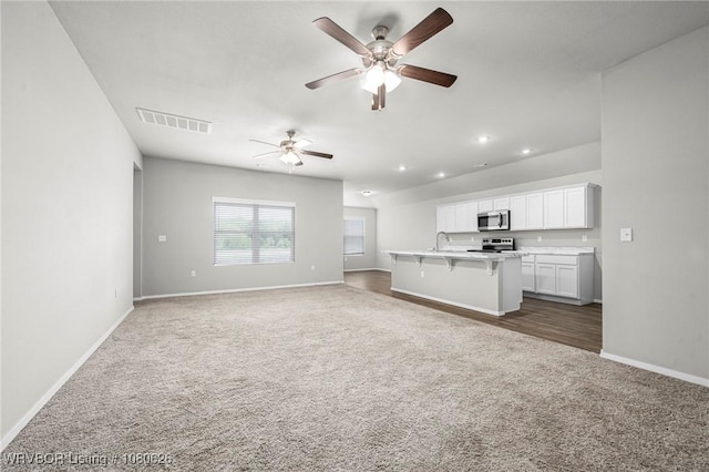 unfurnished living room with baseboards, visible vents, ceiling fan, and dark colored carpet