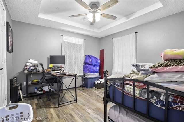 bedroom featuring a tray ceiling, ceiling fan, a textured ceiling, and hardwood / wood-style flooring