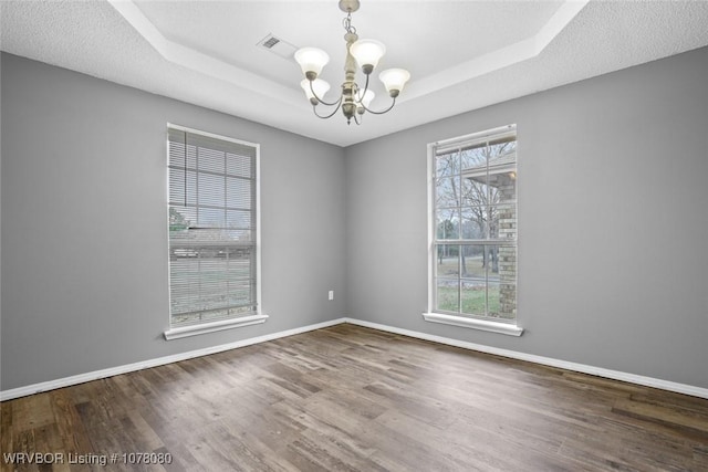 unfurnished room with a raised ceiling, a healthy amount of sunlight, a chandelier, and dark hardwood / wood-style floors