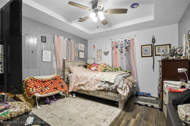 bedroom with a textured ceiling, a tray ceiling, ceiling fan, dark wood-type flooring, and electric panel