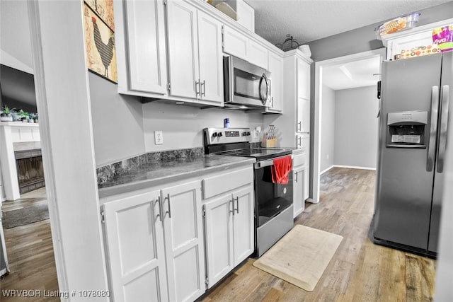 kitchen with white cabinetry, light hardwood / wood-style flooring, stainless steel appliances, and a textured ceiling