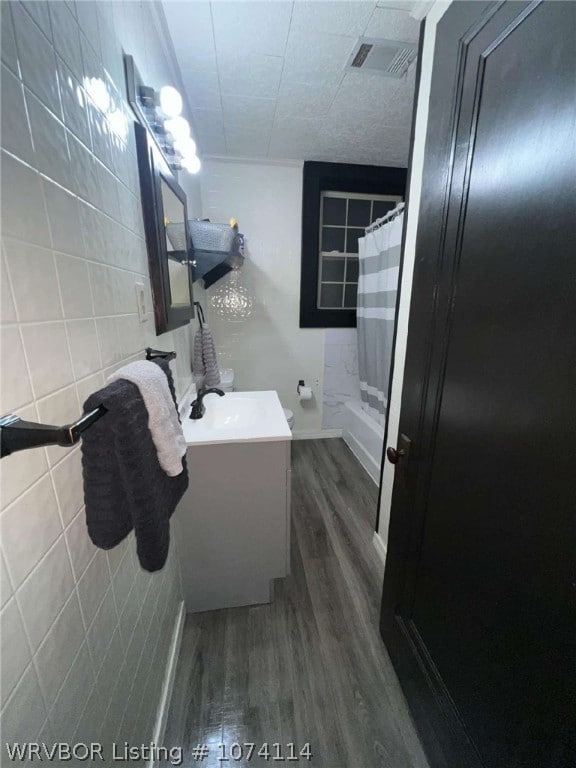 bathroom with hardwood / wood-style floors, shower / bath combination with curtain, tile walls, and vanity