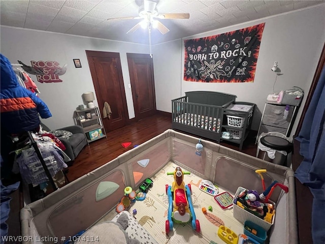 bedroom with a crib, dark hardwood / wood-style flooring, and ceiling fan