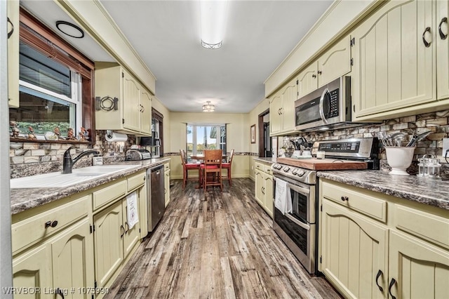 kitchen with sink, light hardwood / wood-style flooring, cream cabinets, decorative backsplash, and appliances with stainless steel finishes