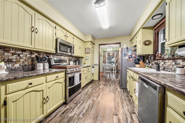 kitchen with hardwood / wood-style floors, backsplash, sink, appliances with stainless steel finishes, and cream cabinetry