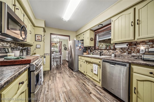 kitchen with decorative backsplash, light wood-type flooring, stainless steel appliances, and an inviting chandelier