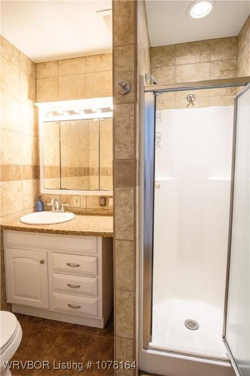 bathroom with toilet, an enclosed shower, tile walls, and vanity