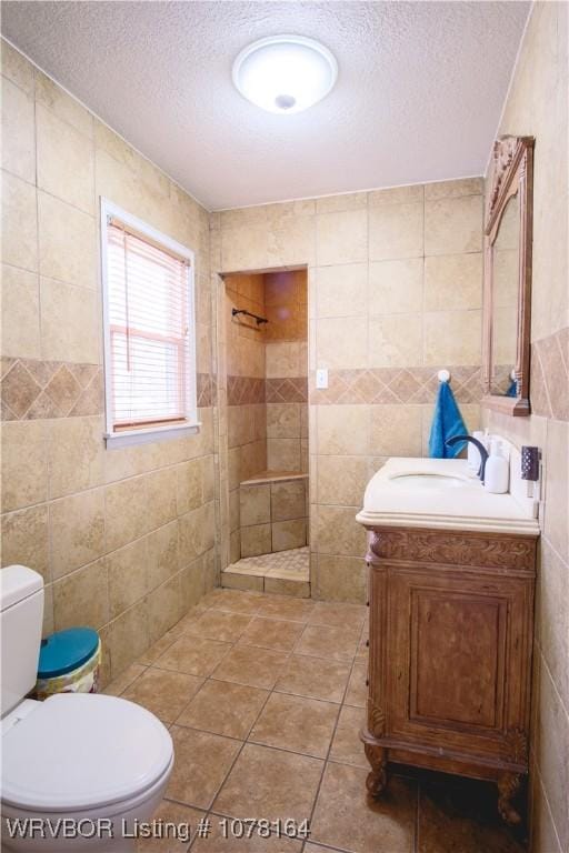 bathroom featuring vanity, toilet, a textured ceiling, tiled shower, and tile walls