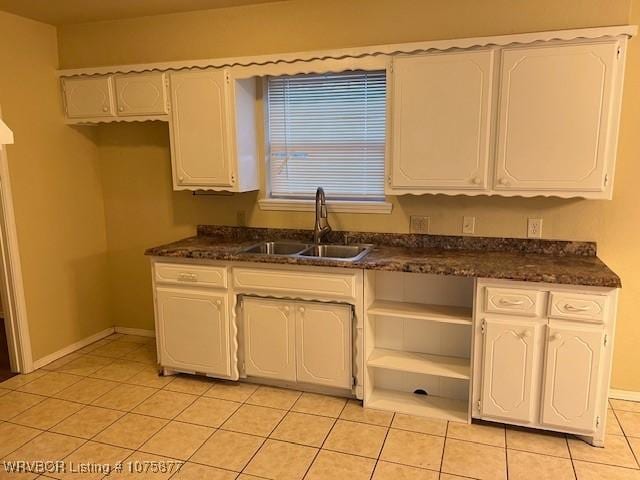 kitchen featuring white cabinets, light tile patterned flooring, dark stone countertops, and sink