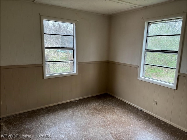 unfurnished room featuring a wainscoted wall, wooden walls, and baseboards