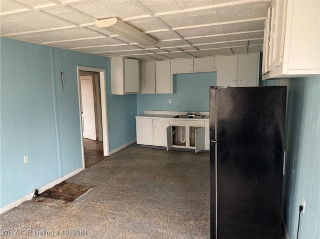 kitchen featuring baseboards, white cabinets, a sink, and freestanding refrigerator