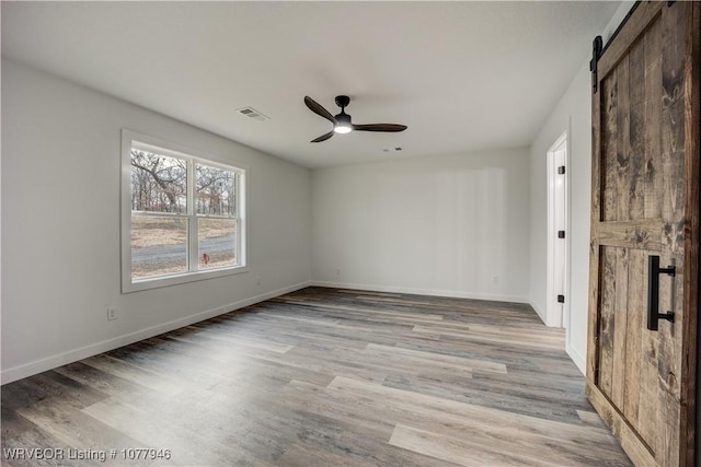 unfurnished room with ceiling fan, a barn door, and light hardwood / wood-style floors