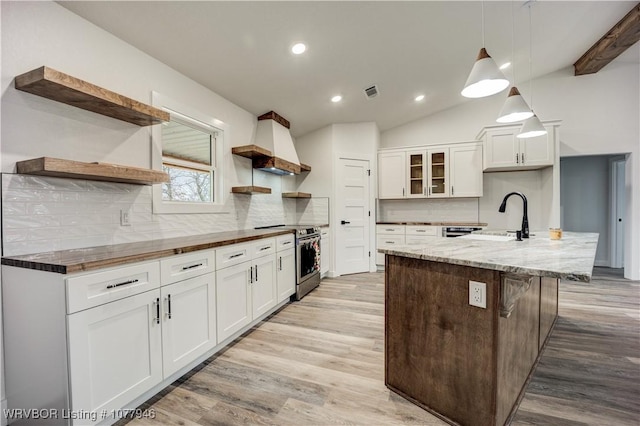 kitchen with electric stove, white cabinets, an island with sink, and custom exhaust hood