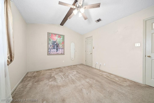 spare room featuring lofted ceiling with beams, ceiling fan, light carpet, and a textured ceiling