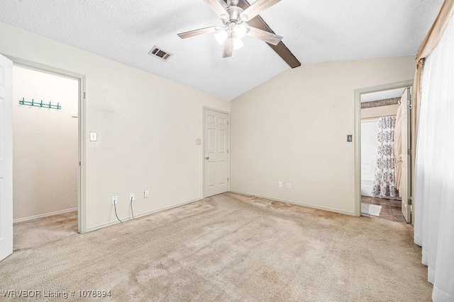 spare room with ceiling fan, vaulted ceiling with beams, light colored carpet, and a textured ceiling