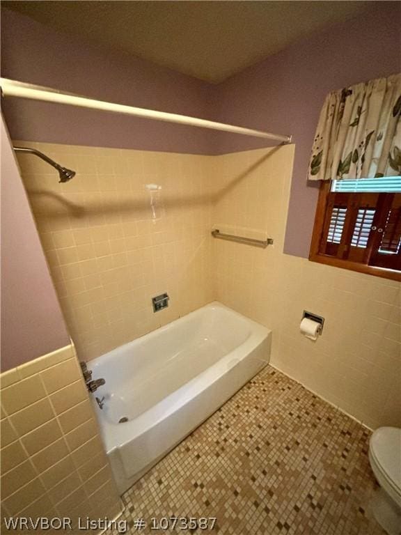 bathroom with toilet, tile patterned floors, tile walls, and washtub / shower combination