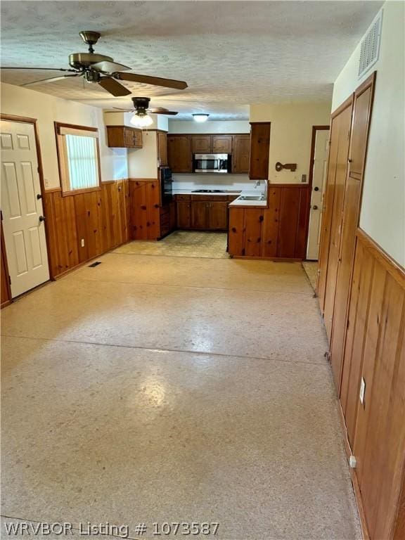 kitchen featuring wood walls, oven, sink, ceiling fan, and a textured ceiling