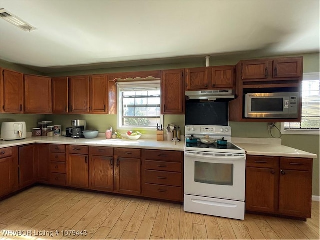 kitchen with under cabinet range hood, white electric range, visible vents, light countertops, and stainless steel microwave