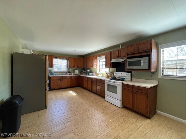 kitchen featuring light wood-style flooring, under cabinet range hood, white appliances, baseboards, and light countertops