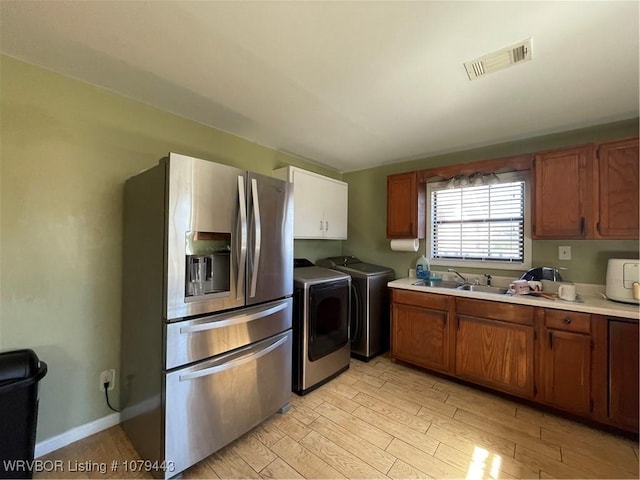 kitchen with a sink, visible vents, independent washer and dryer, stainless steel refrigerator with ice dispenser, and light wood finished floors