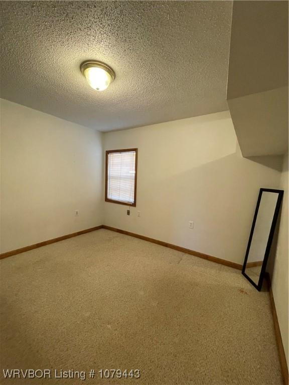 unfurnished room featuring light carpet, baseboards, and a textured ceiling