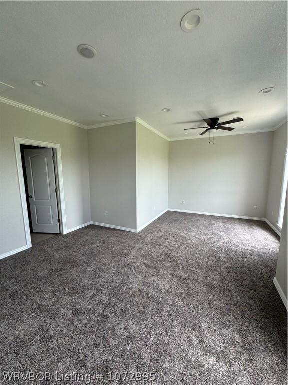 spare room featuring ceiling fan, dark carpet, and ornamental molding