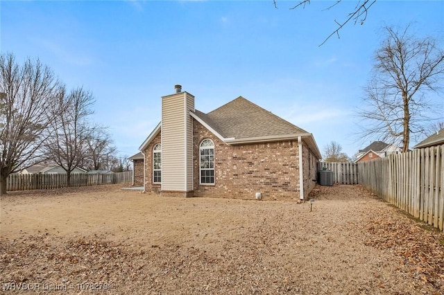 back of house featuring cooling unit, a fenced backyard, brick siding, a shingled roof, and a chimney