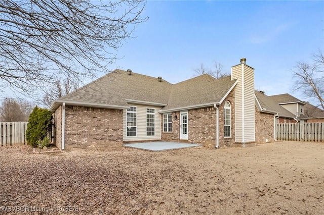 rear view of property with a fenced backyard, a chimney, a patio, and brick siding