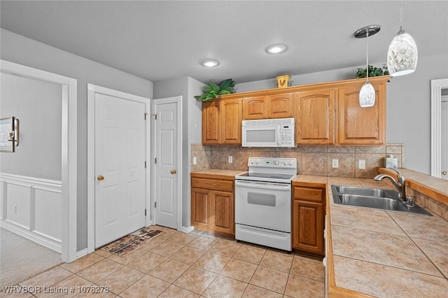 kitchen with light tile patterned floors, tile counters, hanging light fixtures, a sink, and white appliances