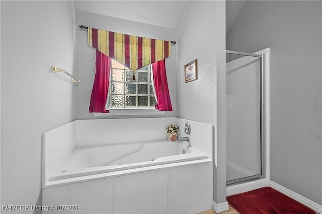 bathroom featuring a stall shower, a bath, and baseboards