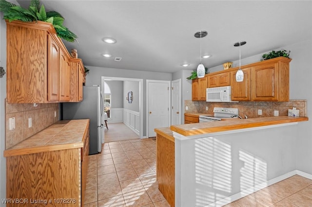 kitchen with a peninsula, white appliances, tile counters, and decorative light fixtures