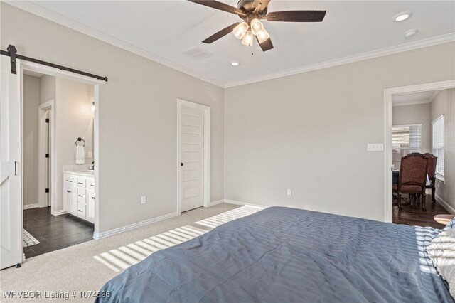 bedroom featuring dark carpet, crown molding, ensuite bath, ceiling fan, and a barn door