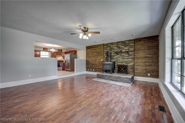 1141 Mountain Grove Ter, Alma, AR 72921 - unfurnished living room featuring a textured ceiling, a wood stove, light wood-type flooring, ceiling fan, and wooden walls
