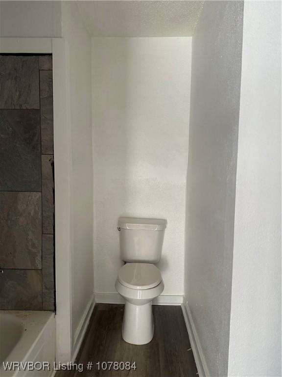 bathroom featuring toilet, a textured ceiling, hardwood / wood-style flooring, and a bathing tub