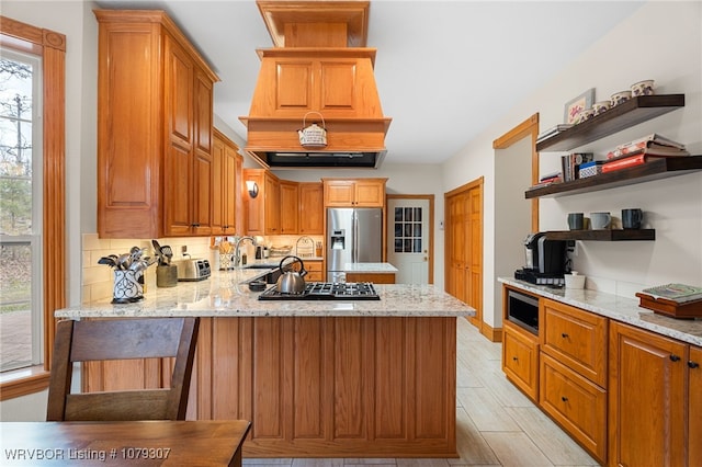 kitchen featuring open shelves, appliances with stainless steel finishes, a sink, light stone countertops, and a peninsula