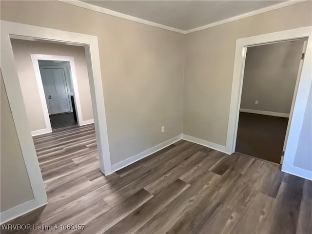 empty room featuring dark wood-type flooring, crown molding, and baseboards